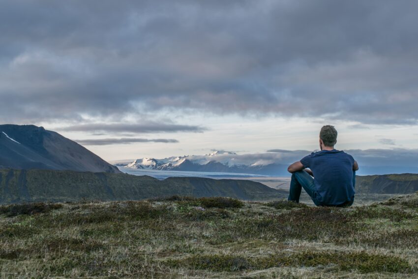 man zittend op berg die uitkijkt op landschap