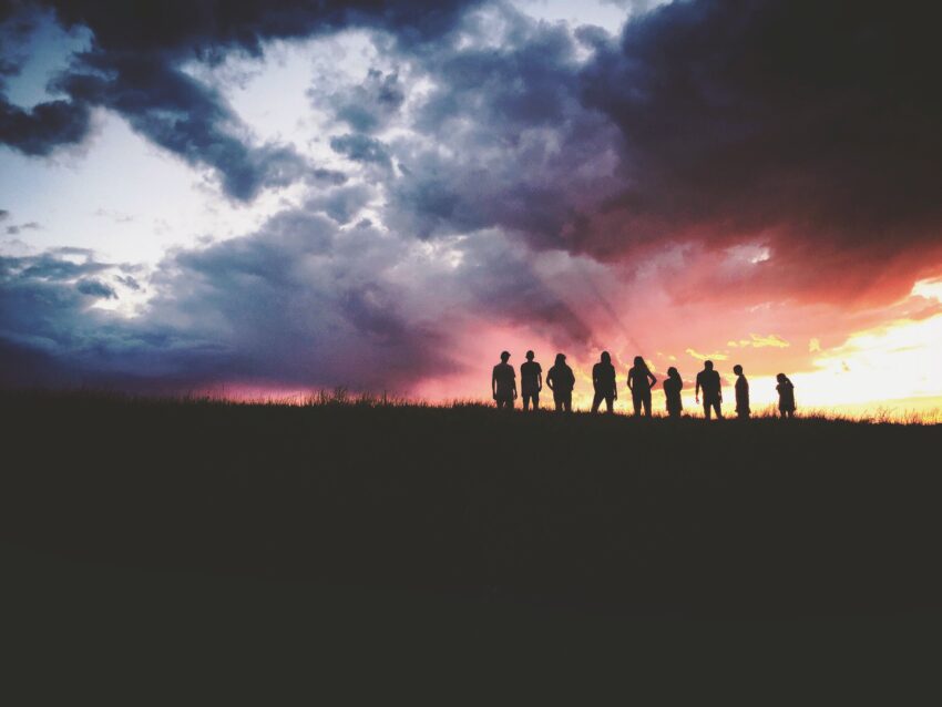 Groep mensen bij zonsondergang op topje van heuvel