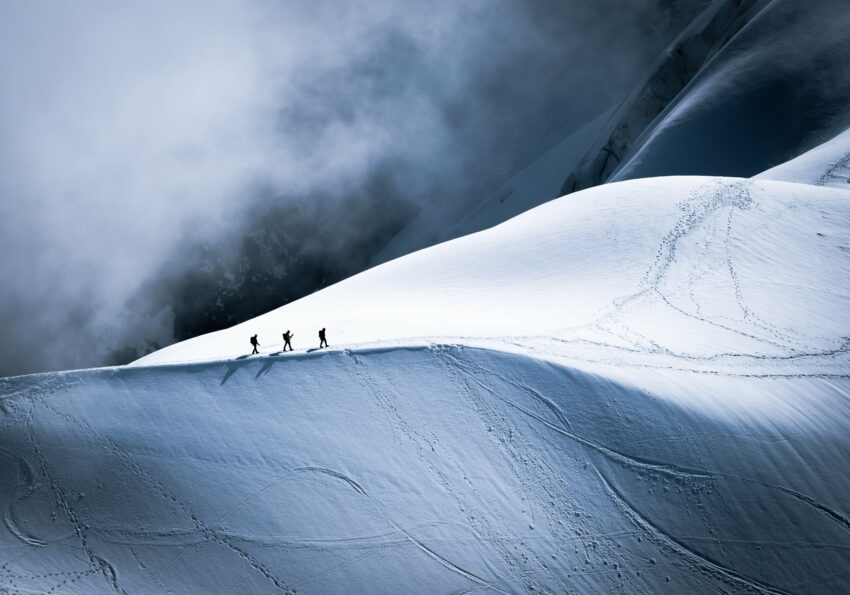 3 bergbeklimmers lopen op de top van besneeuwde bergkam