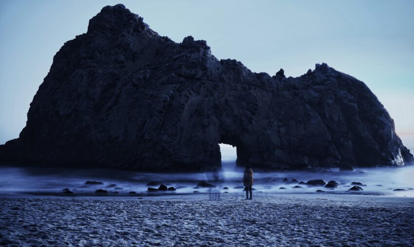 persoon met 2 vervaagde mensen op strand met rots in zee